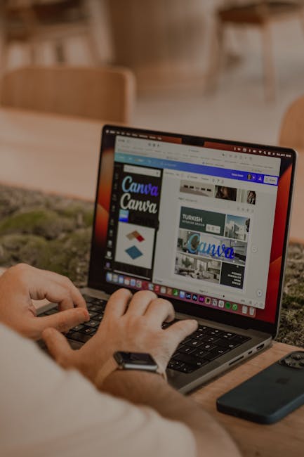 Close-up of hands typing on a laptop displaying graphic design software.